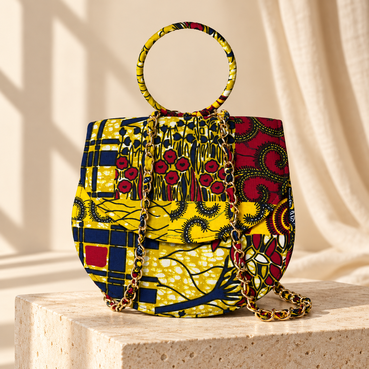 Syda African print Ankara handbag in yellow, burgundy and navy with circular handle and gold-tone chain.