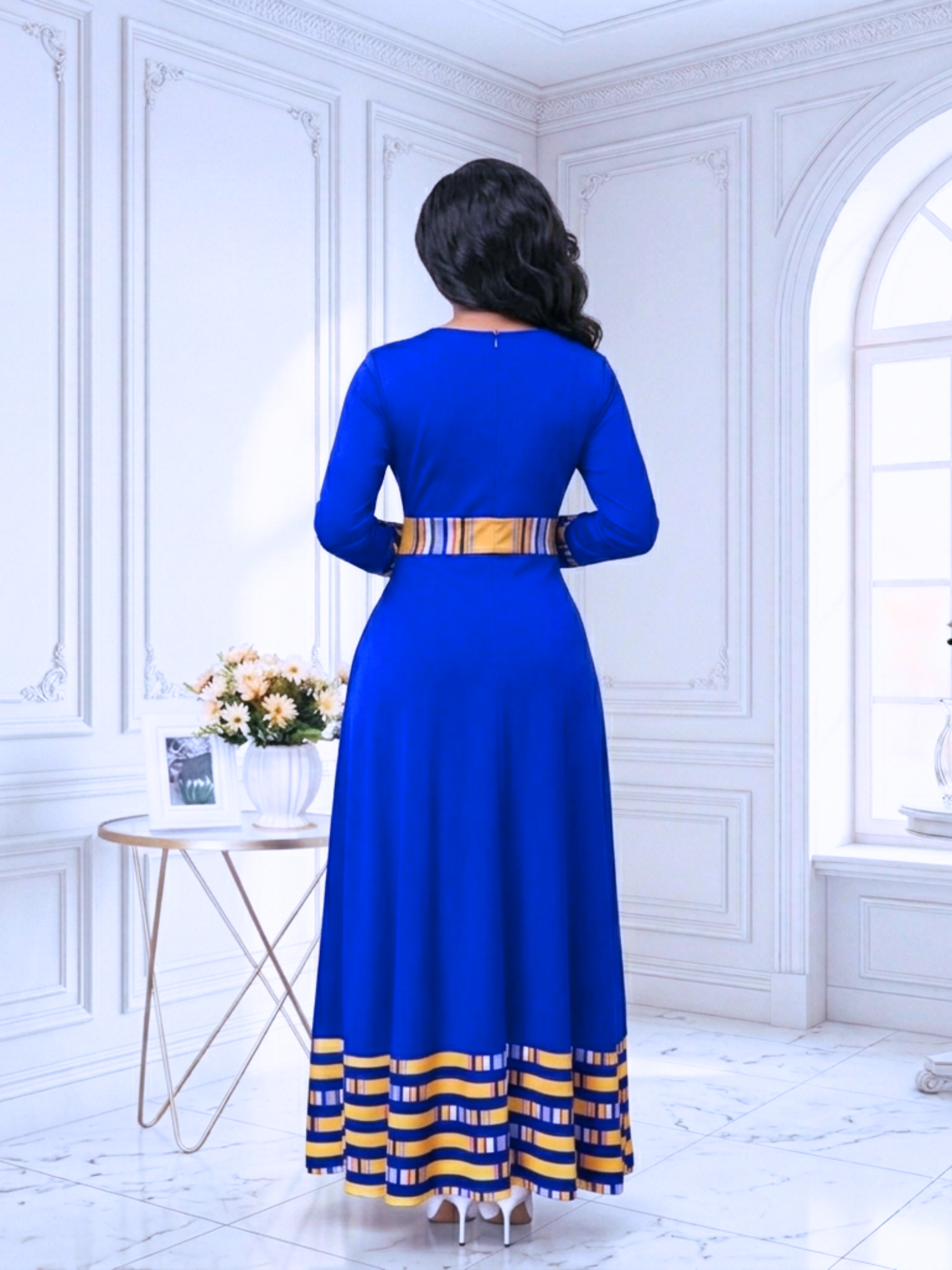 Woman wearing a blue dress with yellow accents in a white room.