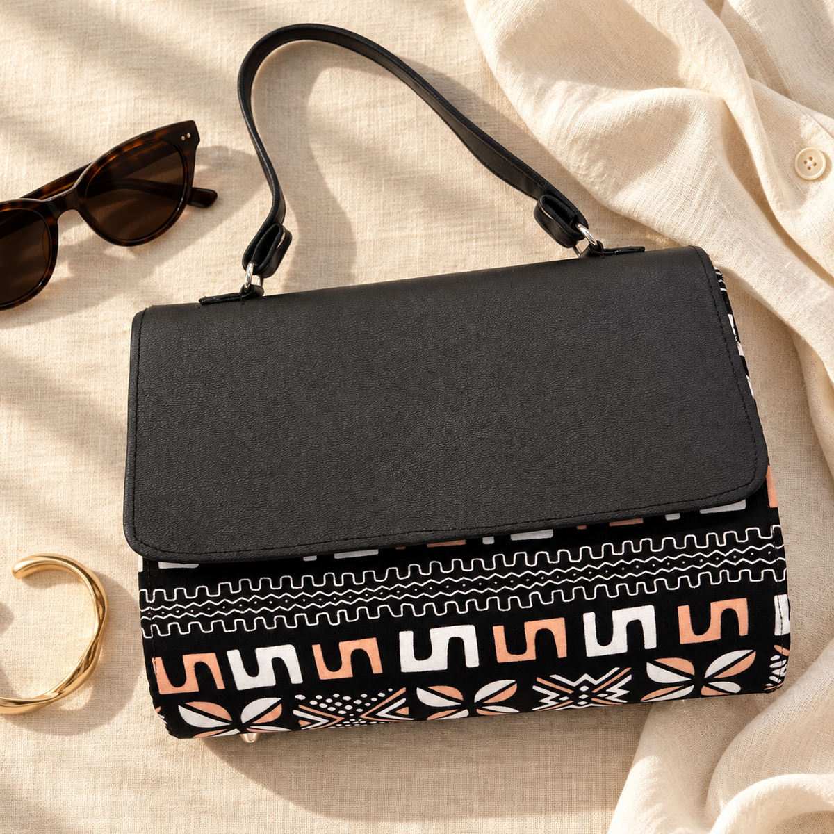 Hananie African mudcloth print handbag with black textured flap and peach-and-white geometric pattern on a cream studio backdrop.